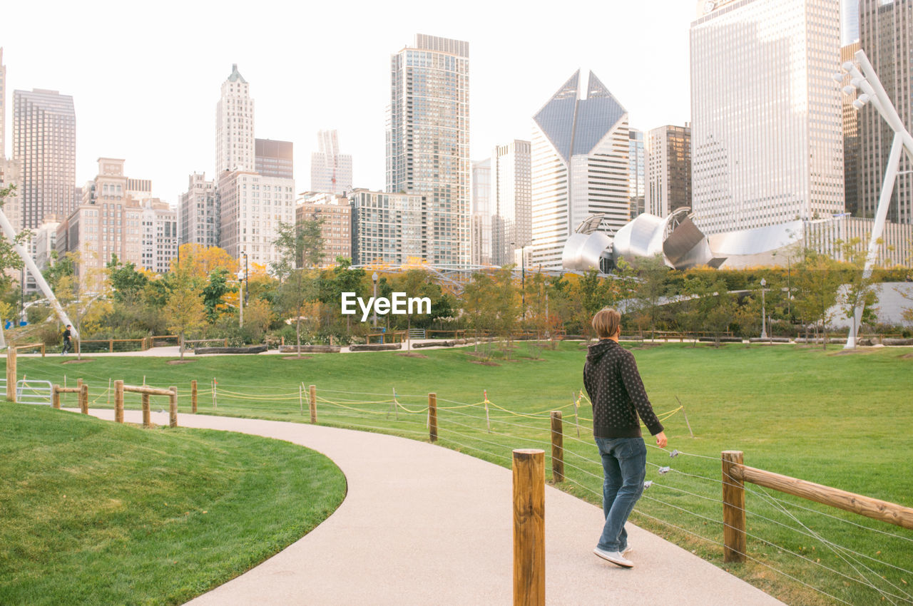 Man on footpath at millennium park against modern buildings in city