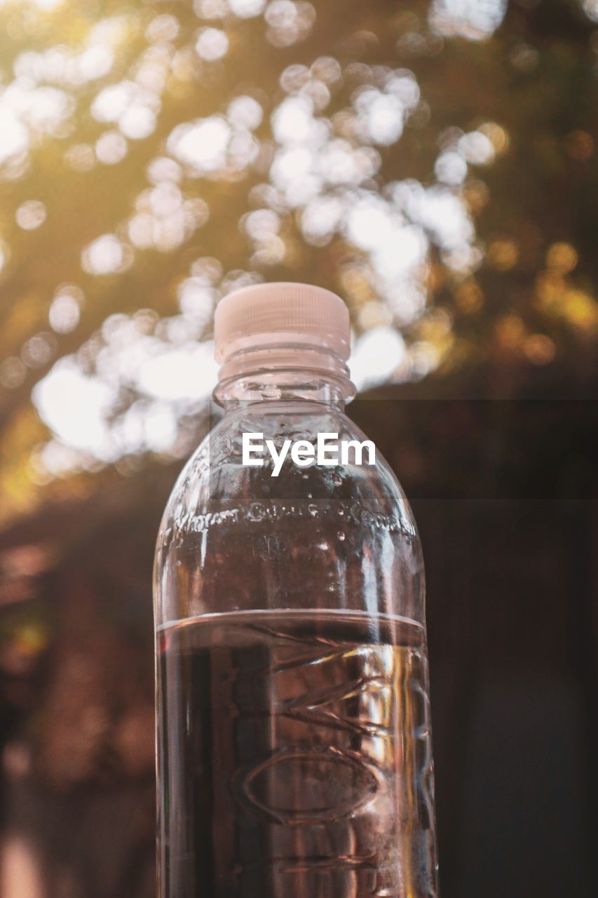 Close-up of water bottle against trees