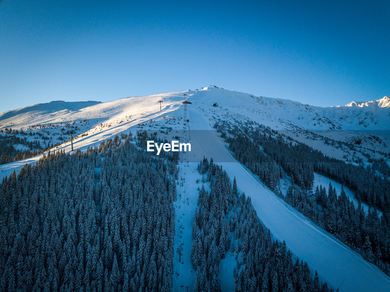 Low angle view of snowcapped mountains against clear blue sky