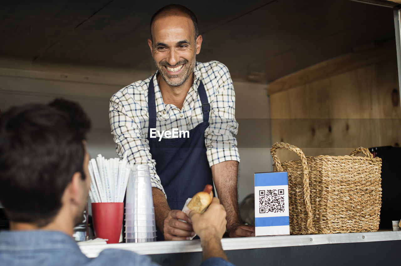 Smiling male vendor giving hotdog to customer at food truck