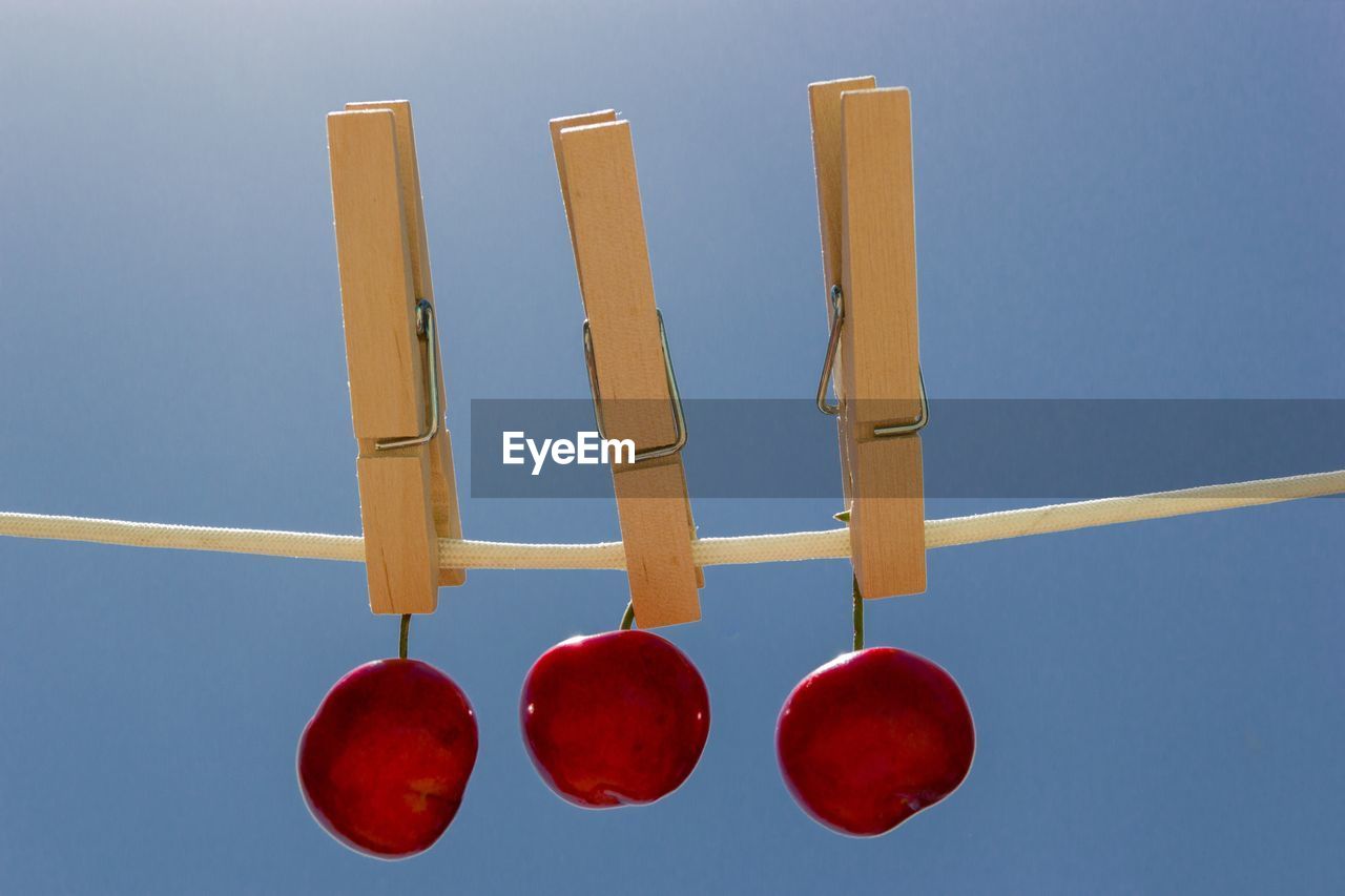 Close-up of cherries hanging with clothespins on rope against clear blue sky