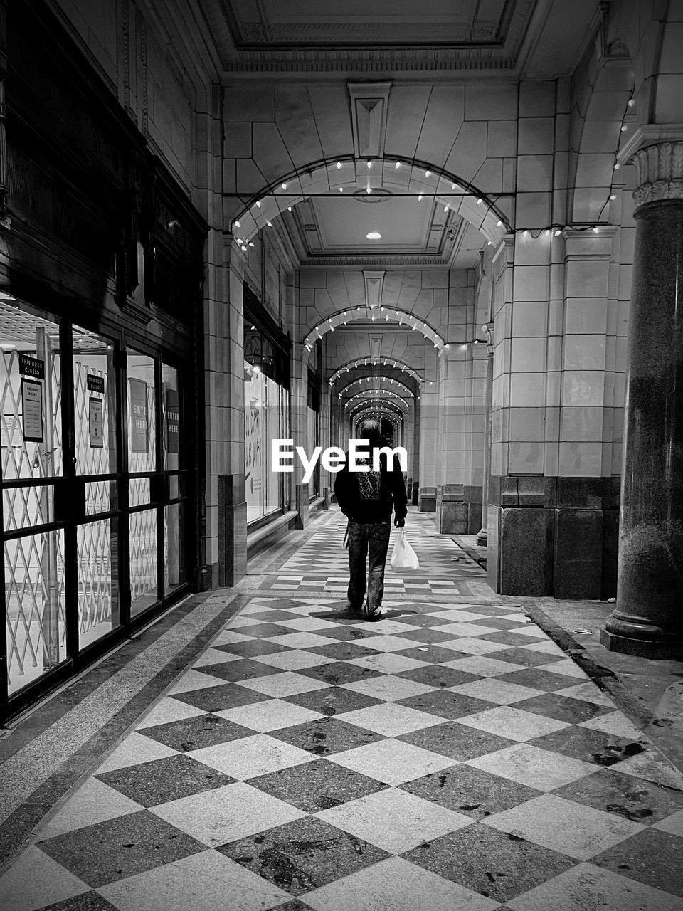 architecture, black and white, full length, monochrome, one person, black, infrastructure, indoors, built structure, rear view, flooring, monochrome photography, tiled floor, tile, adult, road, snapshot, walking, street, the way forward, urban area, men, corridor, arcade, building, darkness, white, lifestyles, footpath