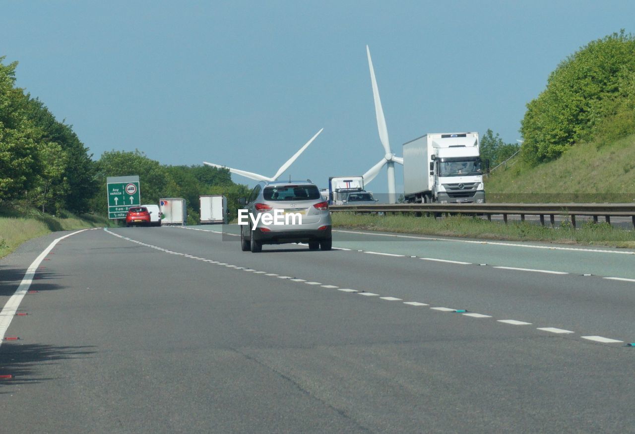 Vehicles on highway with wind turbines against sky