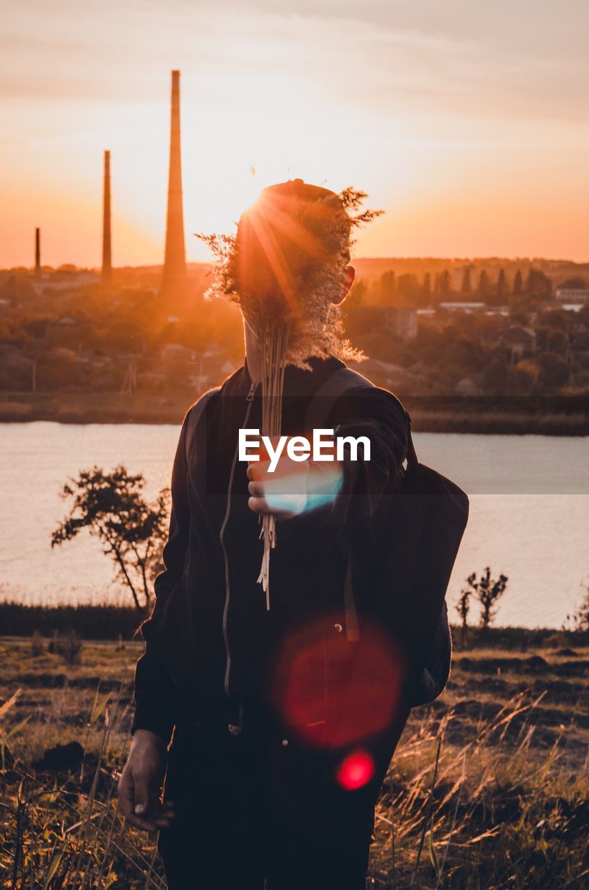 Man holding plant at riverbank during sunset