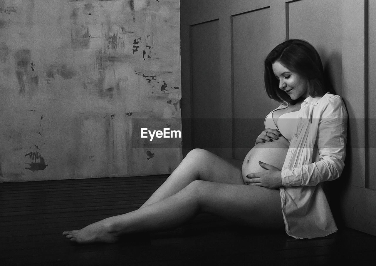 Pregnant woman touching her belly while sitting on hardwood floor at home