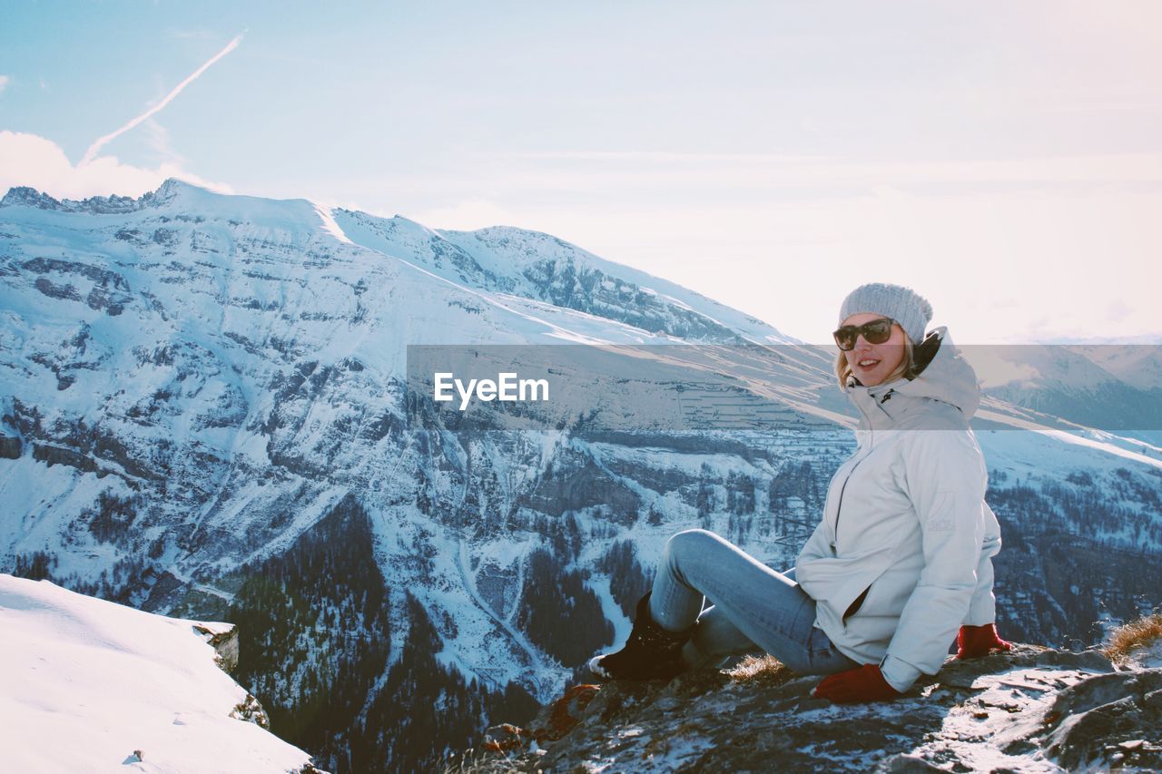 Woman sitting on snow covered mountain against sky