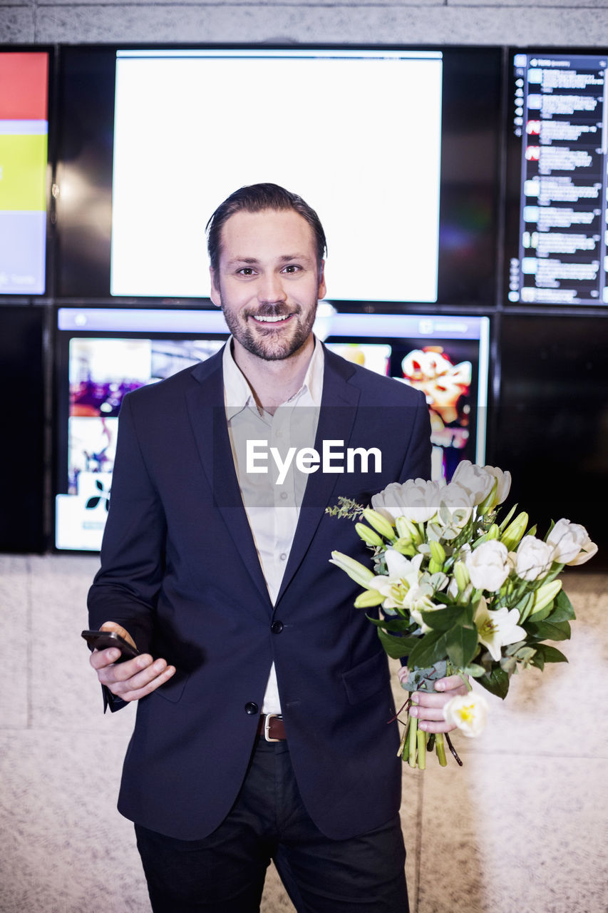 Portrait of successful businessman holding bouquet in office