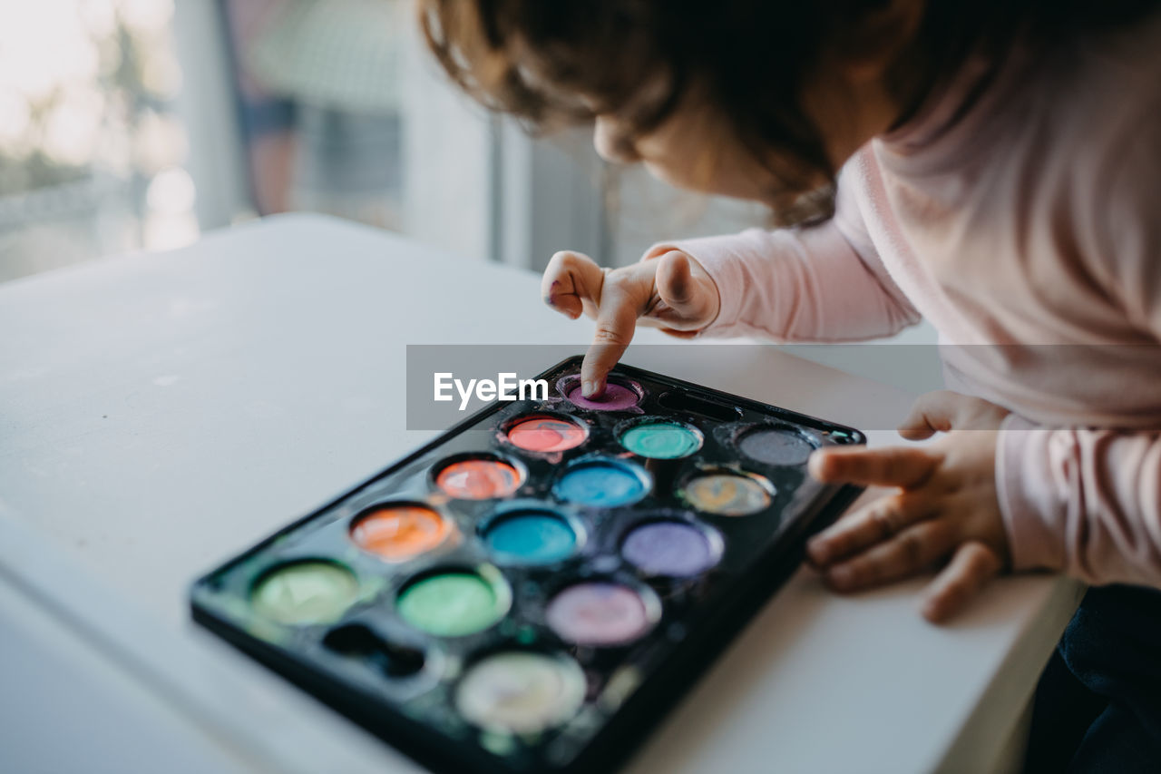 Midsection of girl touching paint in palette
