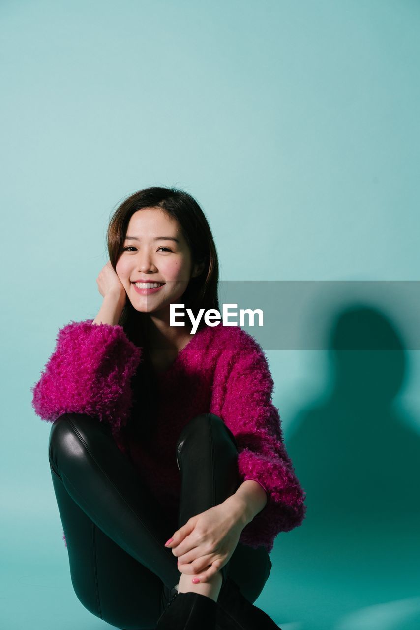 Portrait of smiling young woman sitting against blue background