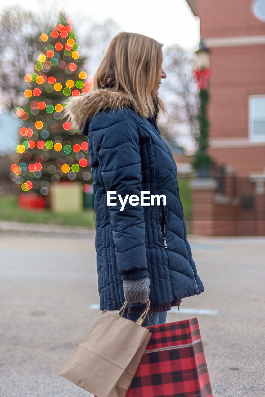 Side view of woman holding shopping bags while standing on road