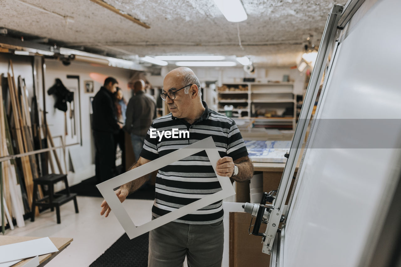 Senior male entrepreneur wearing eyeglasses examining frame in workshop
