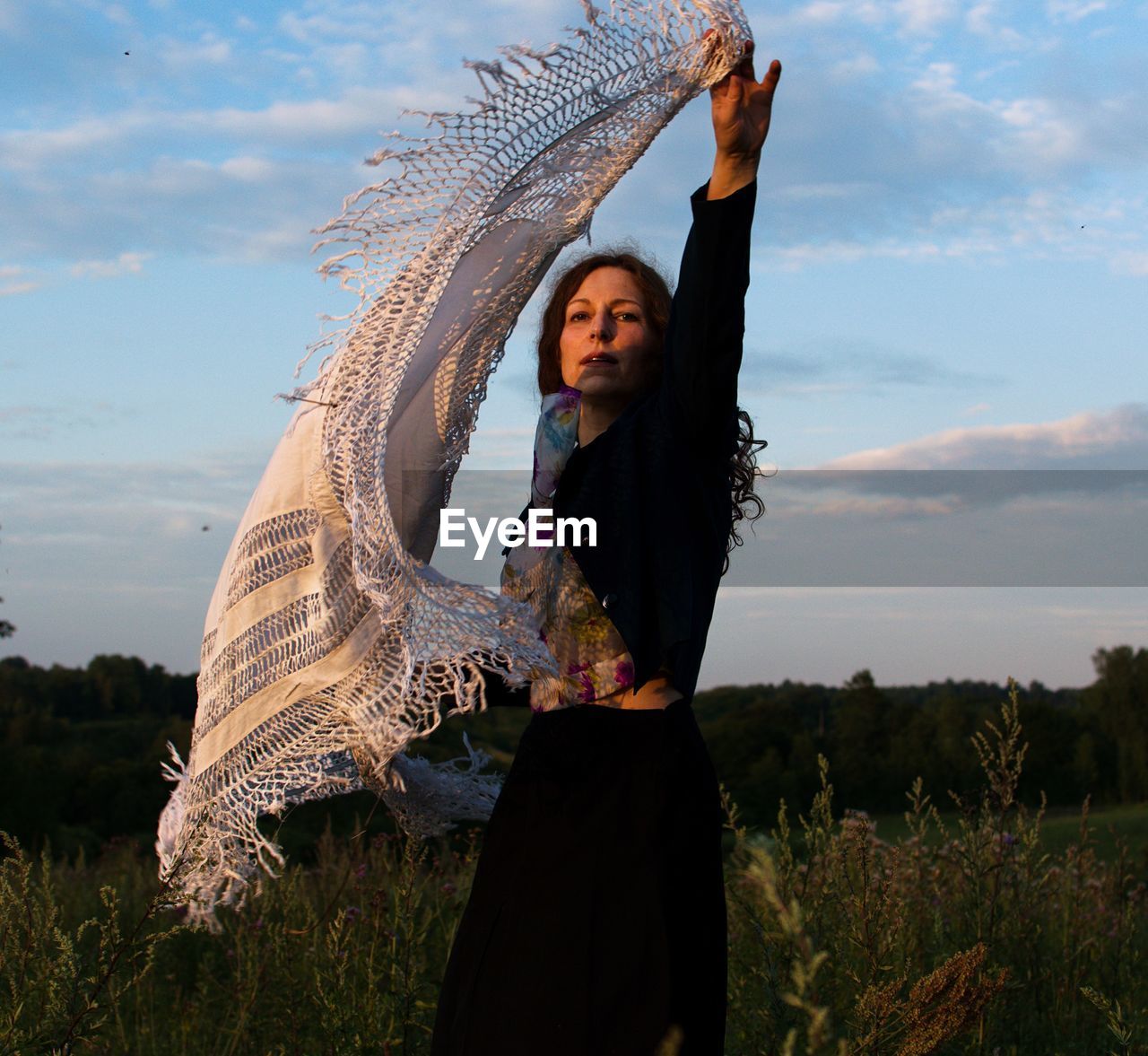 Woman holding scarf while standing against sky