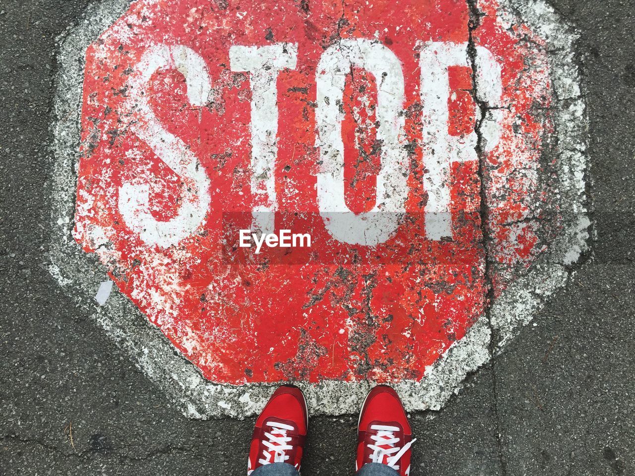 Low section of person standing by stop sign on footpath