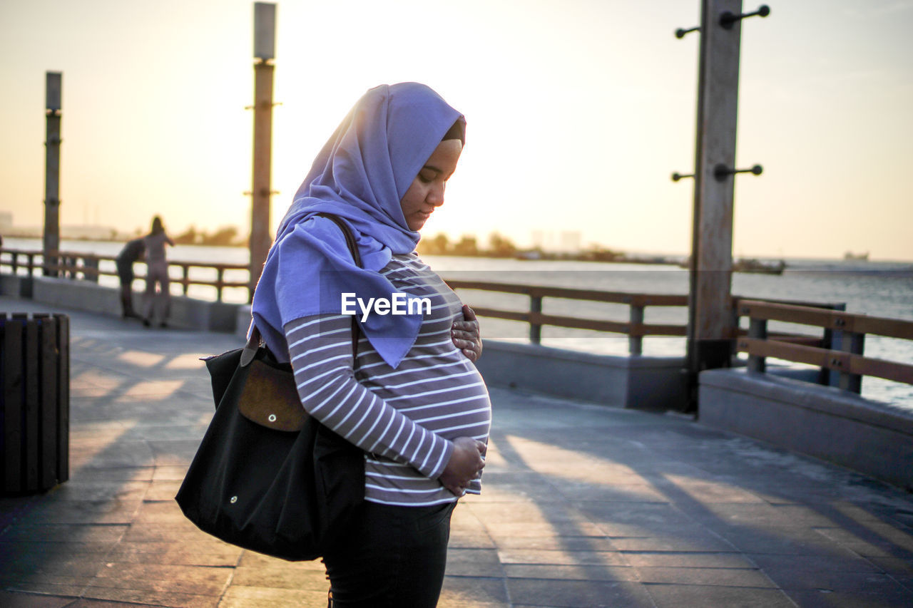 Side view of pregnant woman standing on footpath against sky
