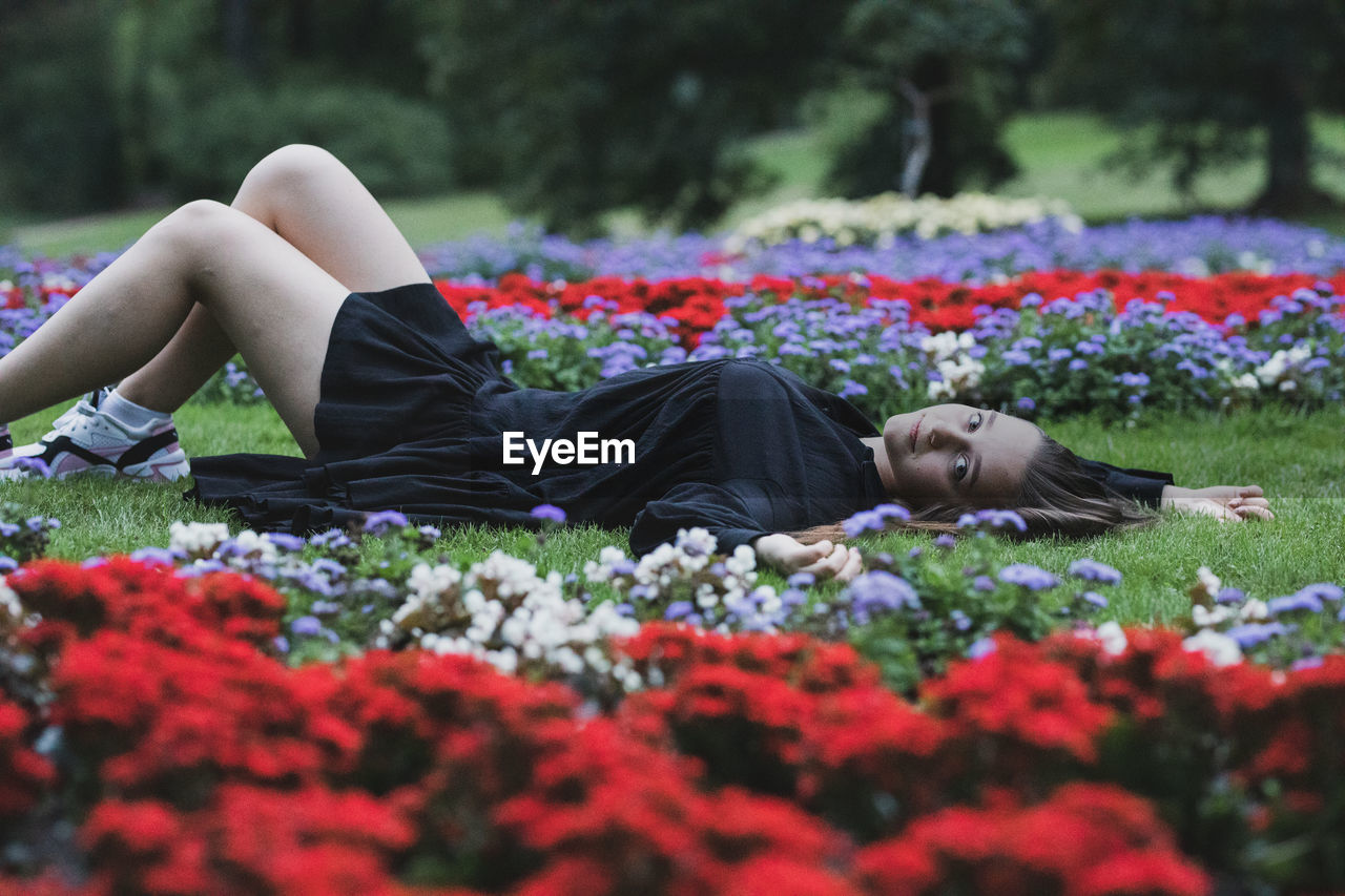 Full length of young woman lying on grass amidst flowering plants