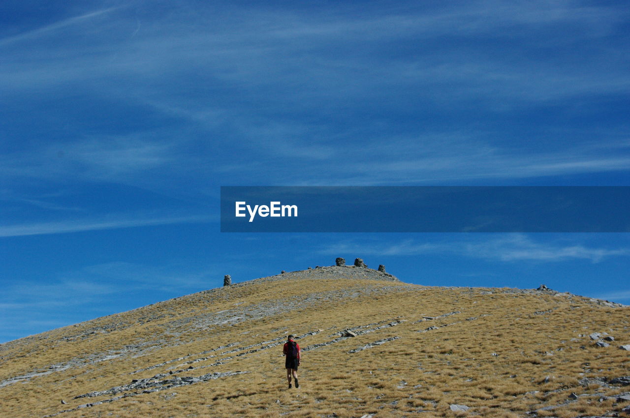 Rear view of man walking on mountain against blue sky