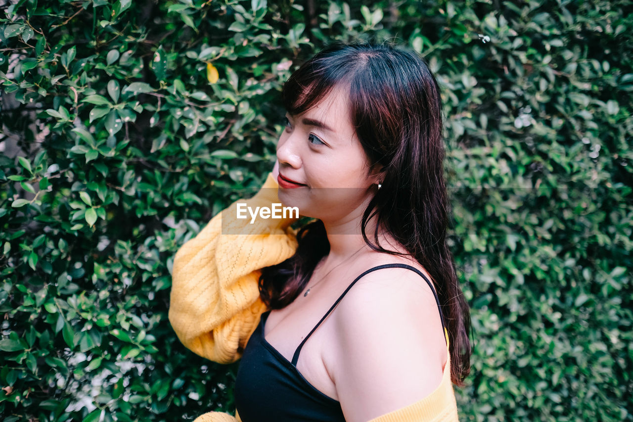 Close up of young pretty asian woman in blue yellow sweater with garden background.