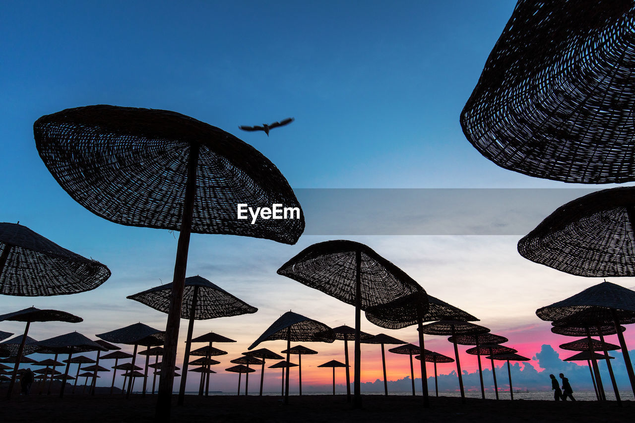 Low angle view of silhouette parasols at beach against sky during sunset