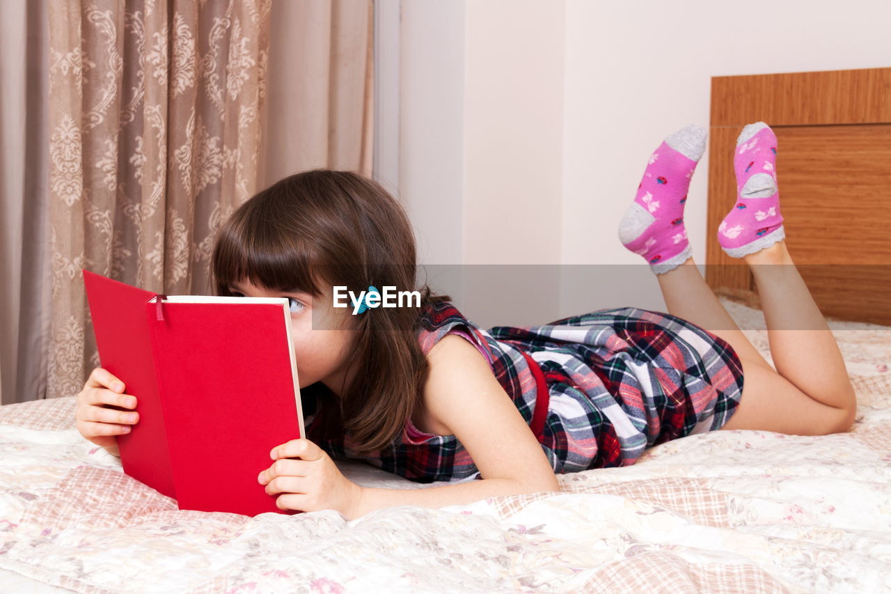 young woman using digital tablet while sitting on bed at home