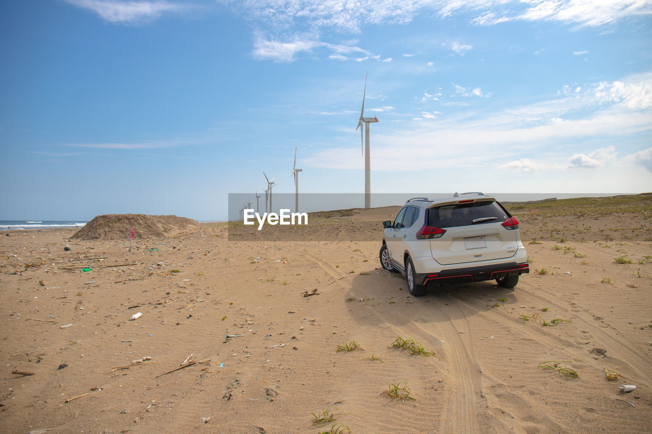 Cars on river side by land against windmills