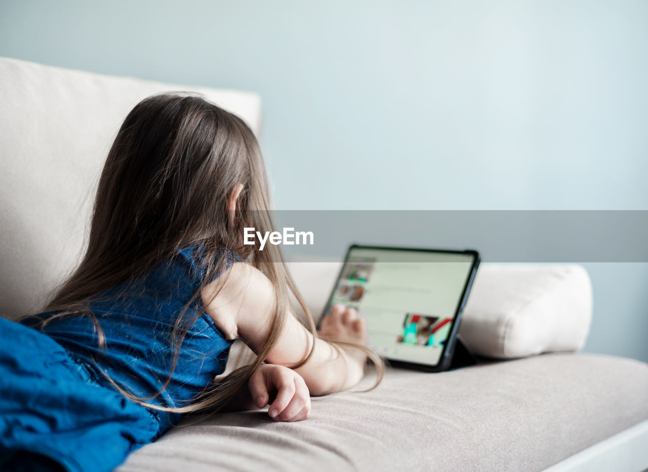 Girl watching video over digital tablet while lying on sofa