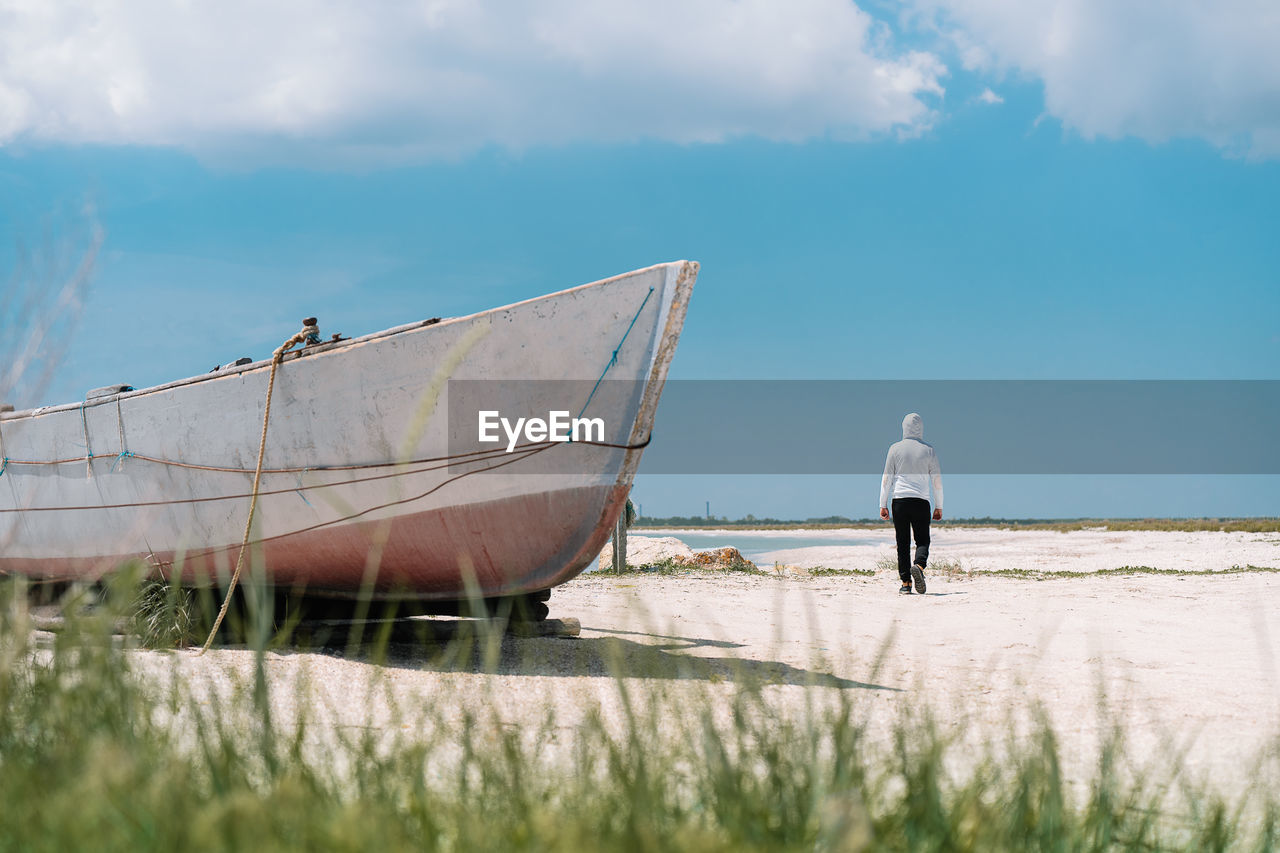 Rear view of man walking on the beach by boat against sky in summer
