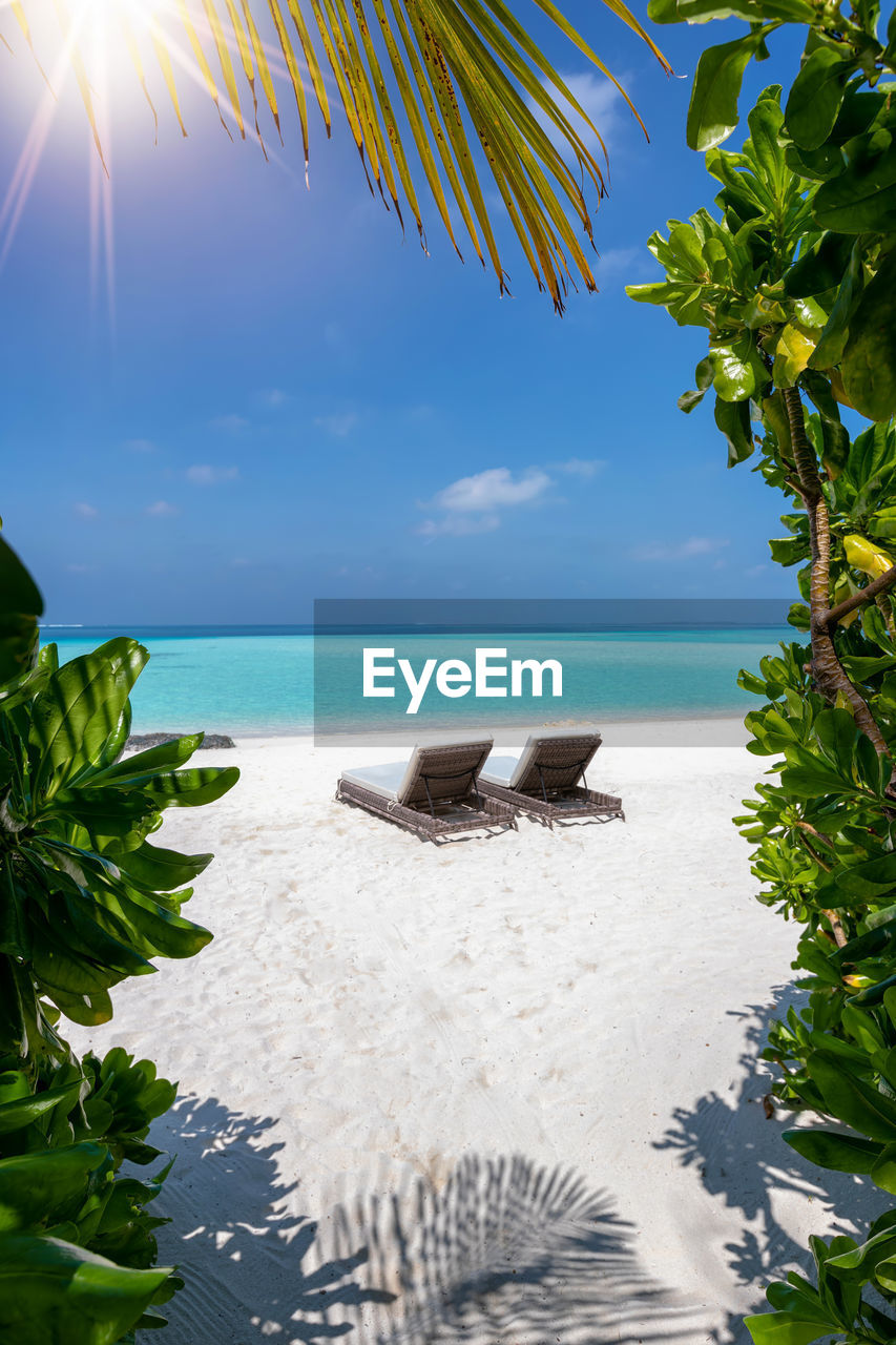 Empty lounge chairs at beach against blue sky