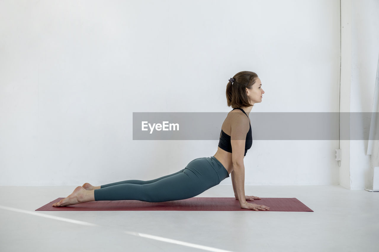Millennial athletic girl in workout sportswear doing stretching yoga in apartment in morning. person