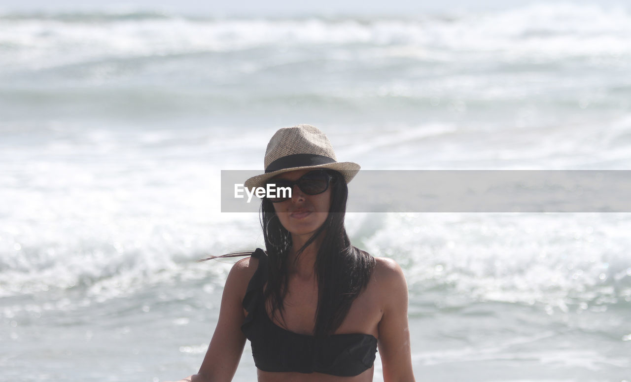 Portrait of young woman wearing sunglasses while standing in sea during sunny day