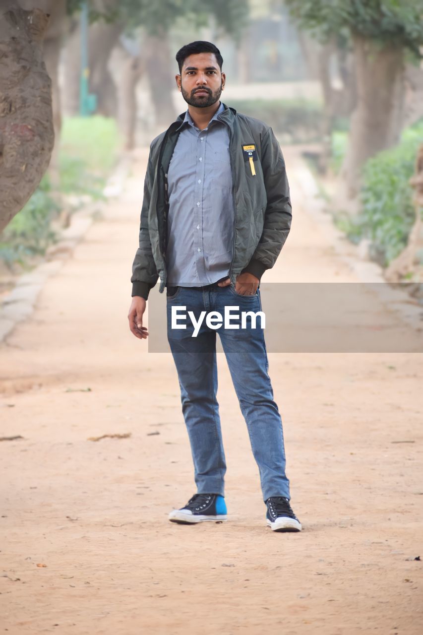 one person, men, adult, full length, portrait, casual clothing, spring, young adult, front view, standing, nature, clothing, lifestyles, jeans, looking at camera, beard, denim, facial hair, tree, smiling, photo shoot, outdoors, emotion, person, land, day, hands in pockets, road, happiness, leisure activity, walking, jacket, looking, copy space, city, fashion, serious, forest