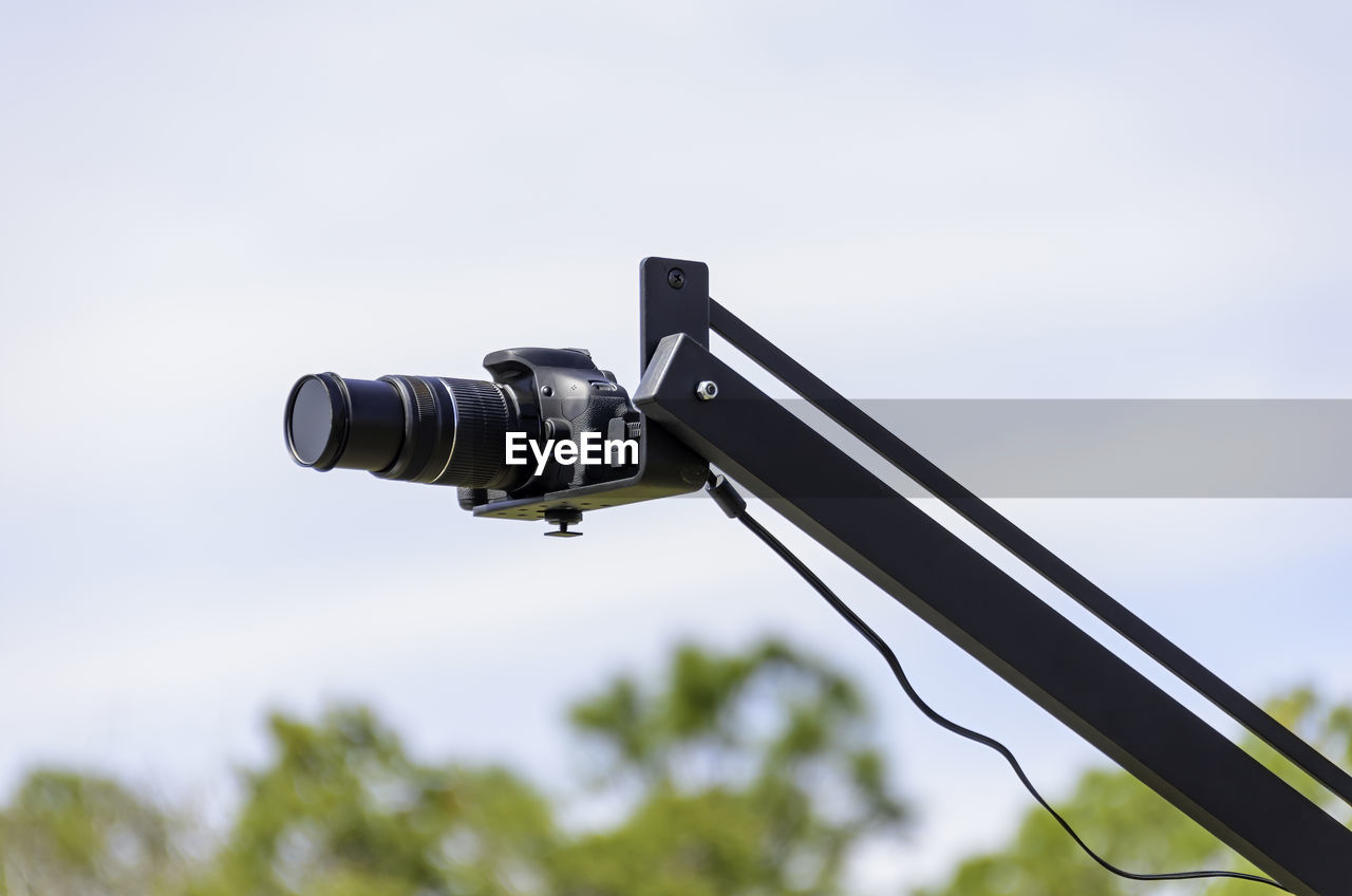 LOW ANGLE VIEW OF CAMERA ON POLE AGAINST SKY