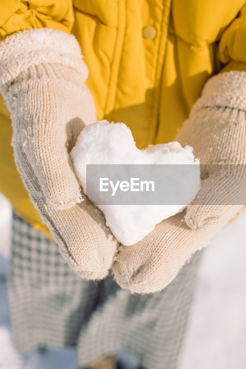 Midsection of woman holding heart shaped snow outdoors