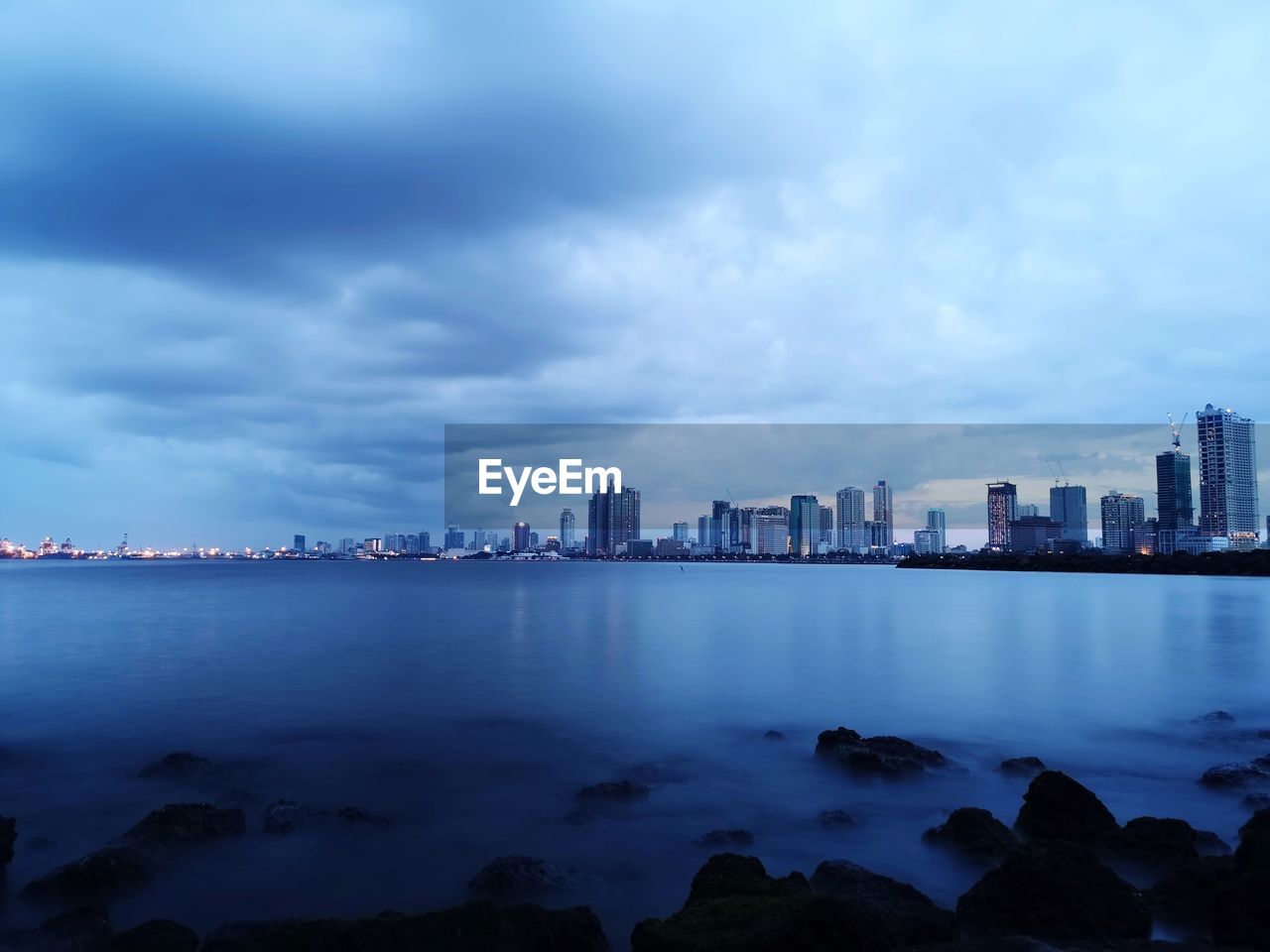 Buildings by sea in city against sky