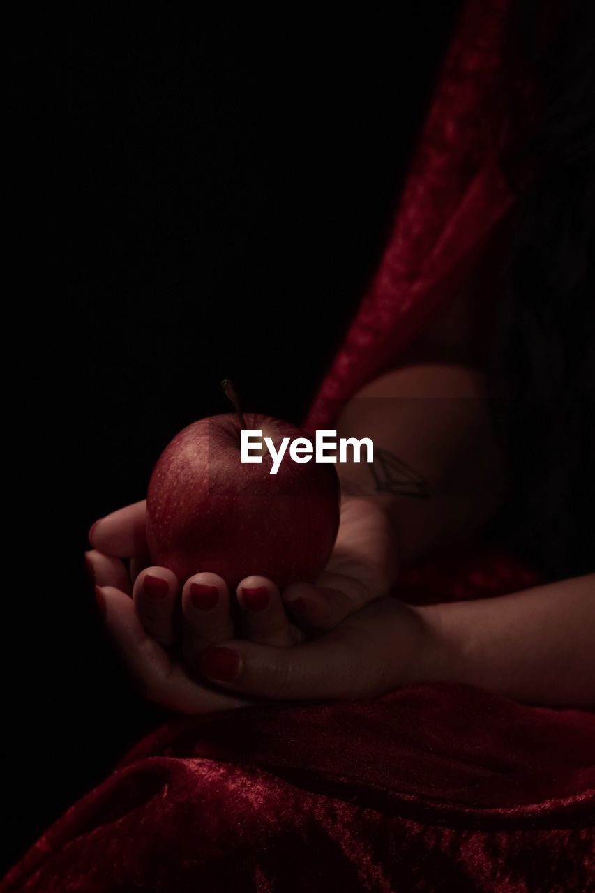 Cropped hands holding apple against black background