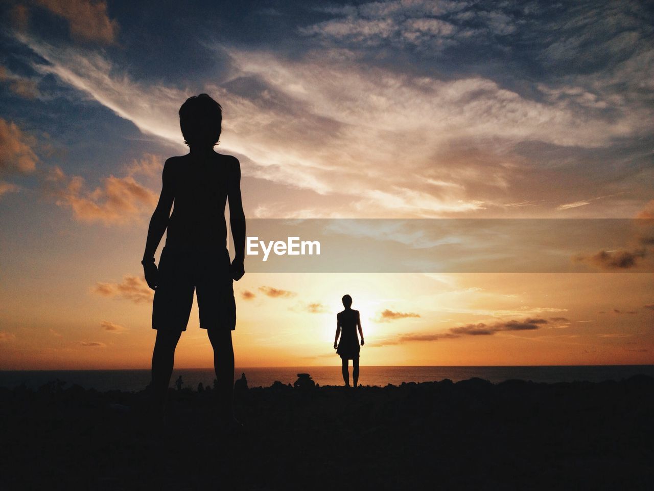 Silhouette boys standing at beach against sky during sunset