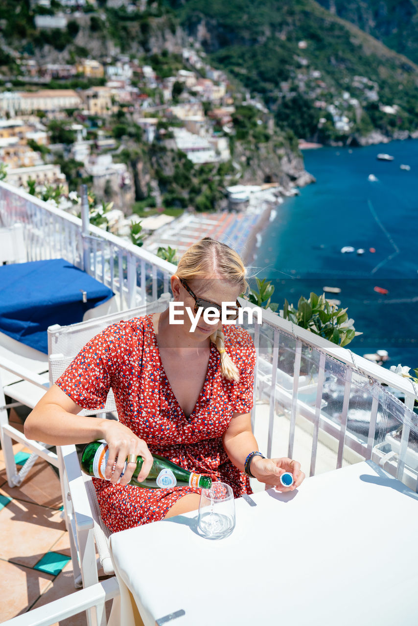 Woman pouring beer in glass while sitting at restaurant against sea