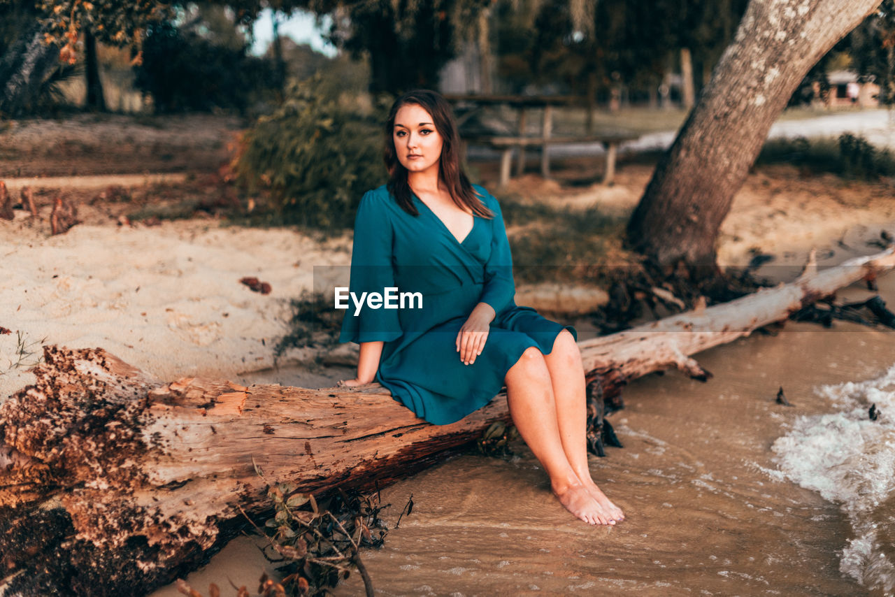 Full length portrait of young woman sitting on wood at beach