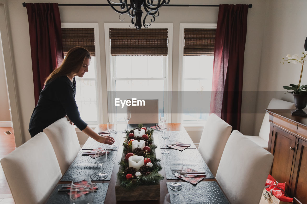 Woman placing a glass on a dining table set for a holiday dinner.