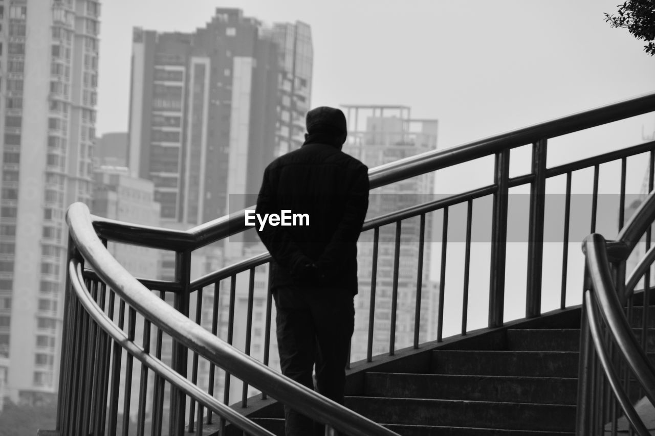 Rear view of man standing on staircase in city against sky