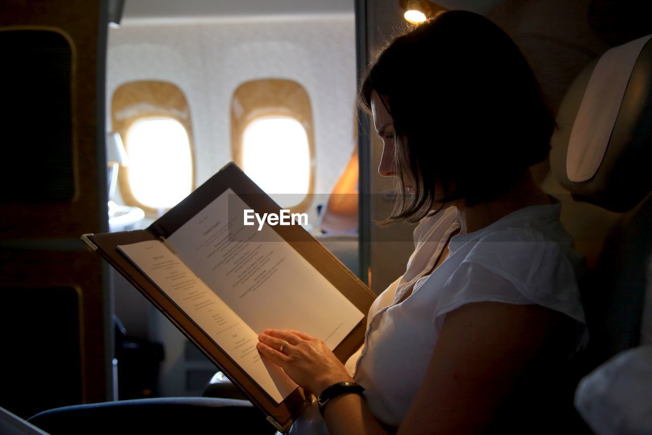 Side view of woman reading menu in airplane