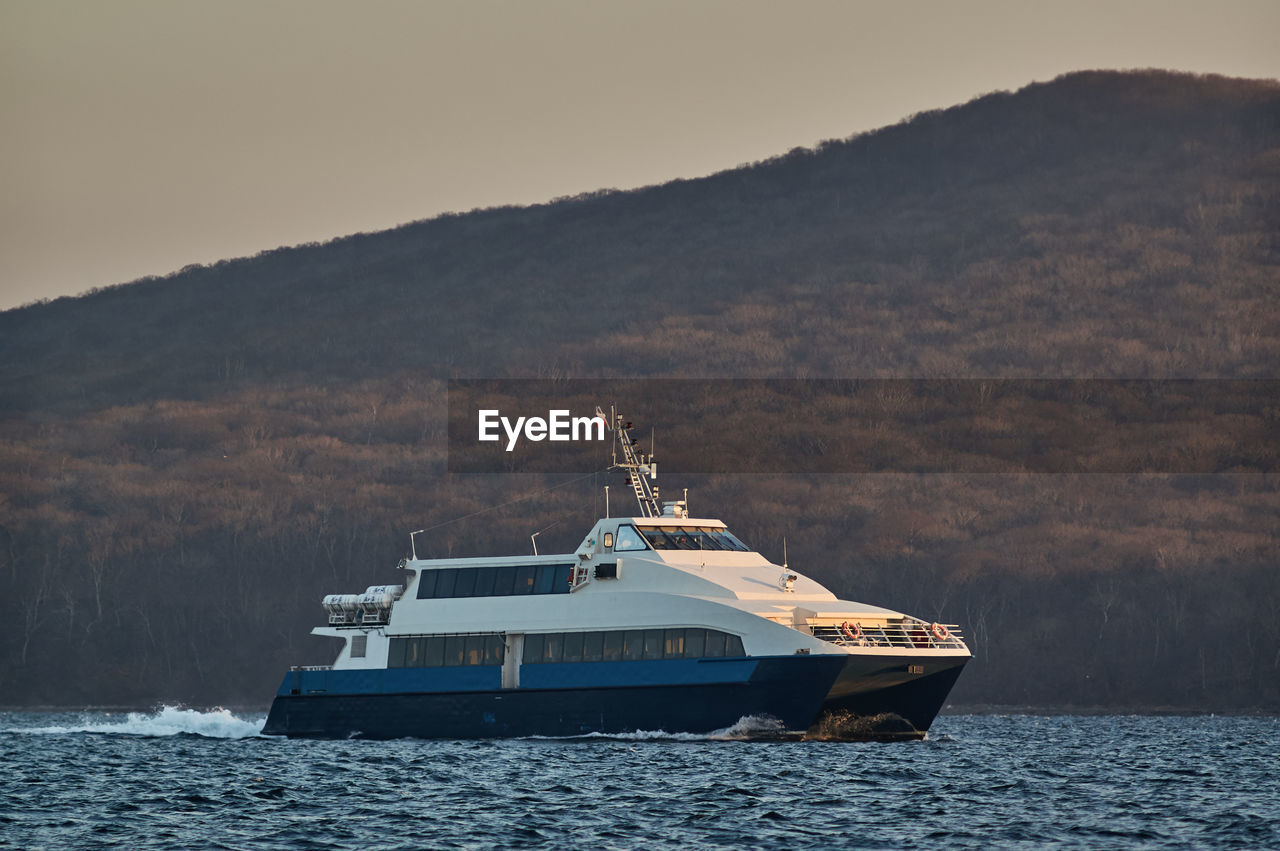 BOAT SAILING ON SEA AGAINST MOUNTAIN