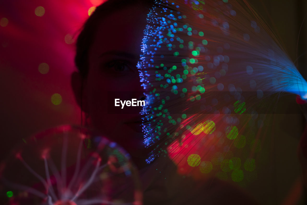 Portrait of beautiful young woman against illuminated background