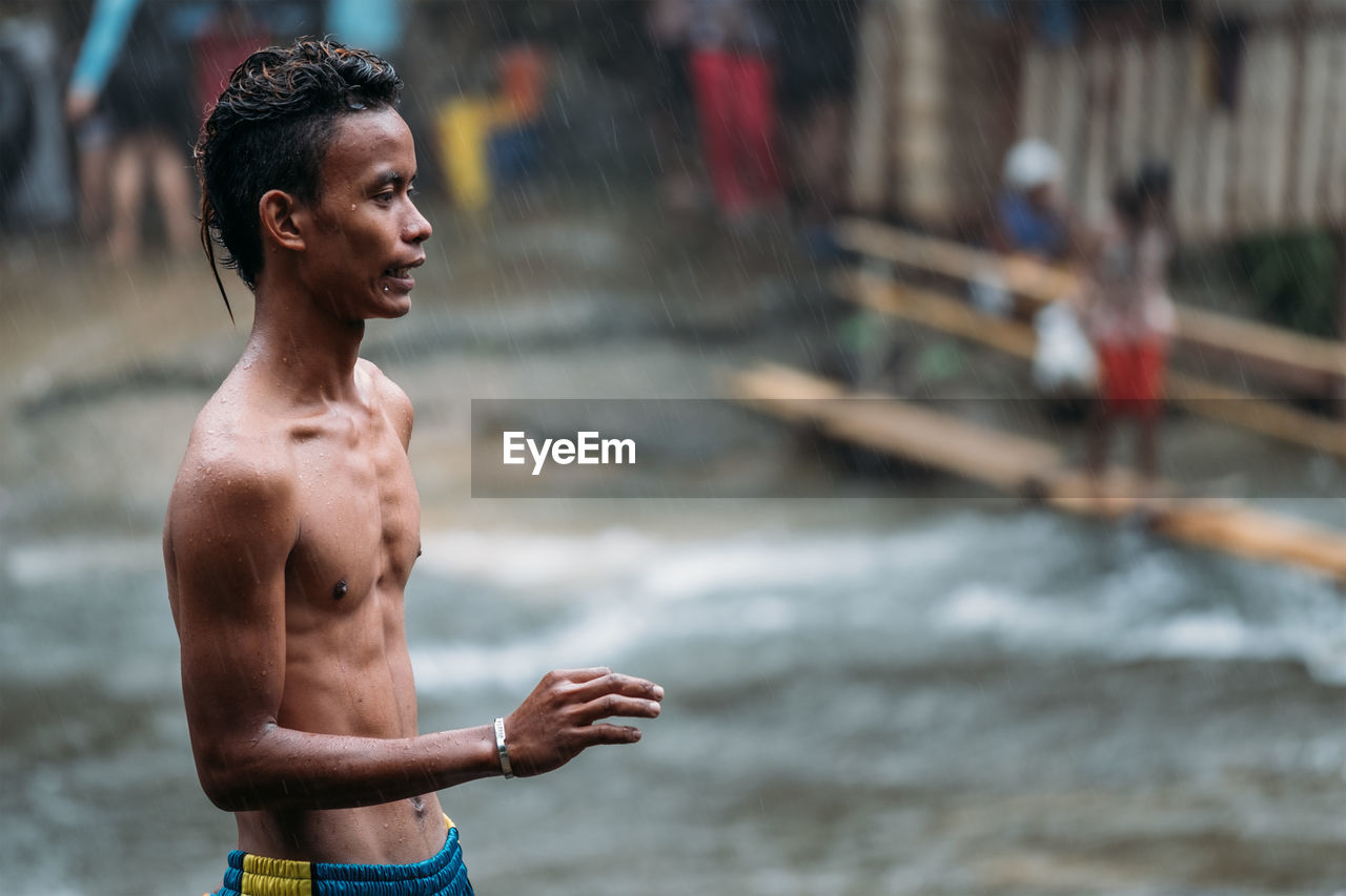 Side view of shirtless man standing on field during rain