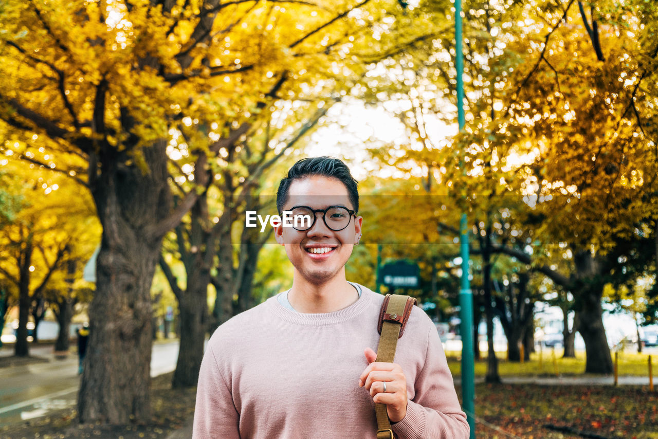 PORTRAIT OF SMILING YOUNG MAN STANDING AGAINST PLANTS