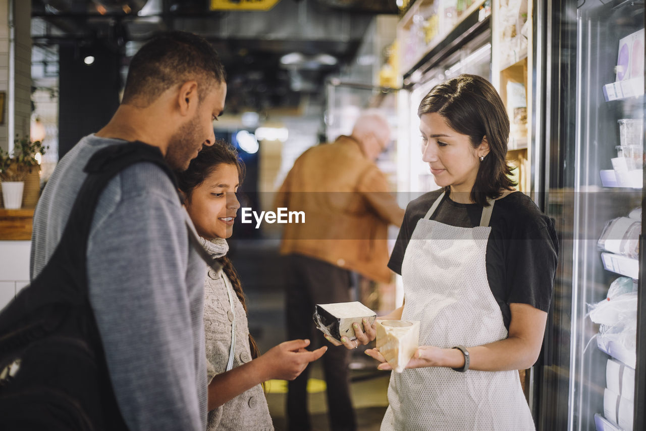 Saleswoman showing cheese to customers at store