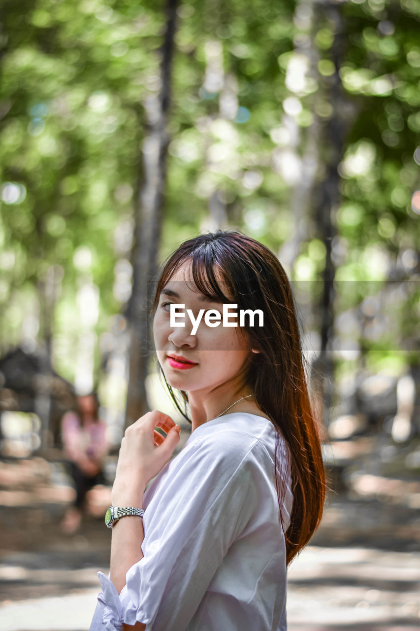 PORTRAIT OF YOUNG WOMAN AGAINST TREES