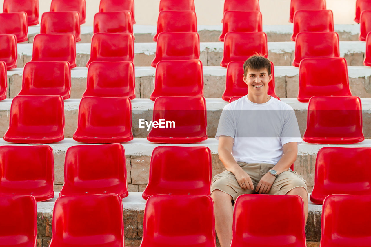 Wide smiling man  is sitting in deserted audience with red seats. absence of people 