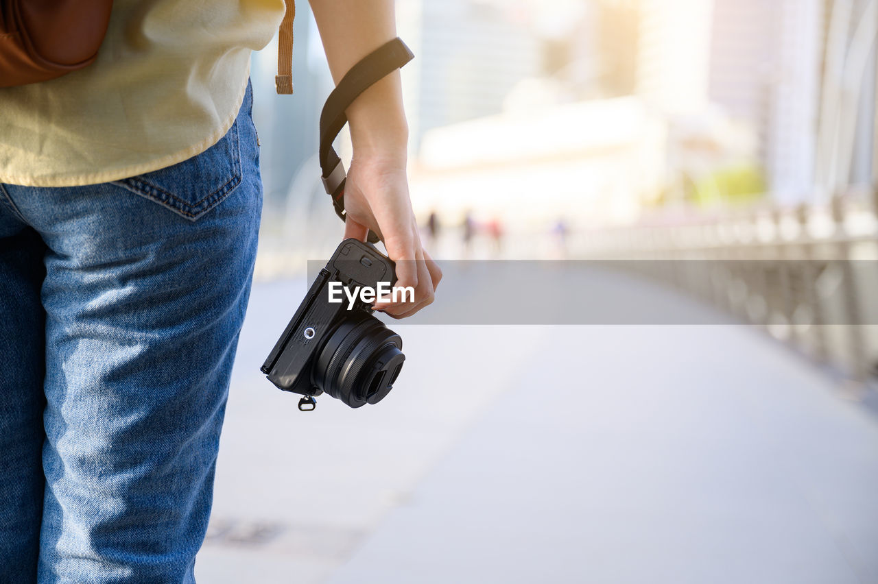 Midsection of woman holding camera while standing outdoors