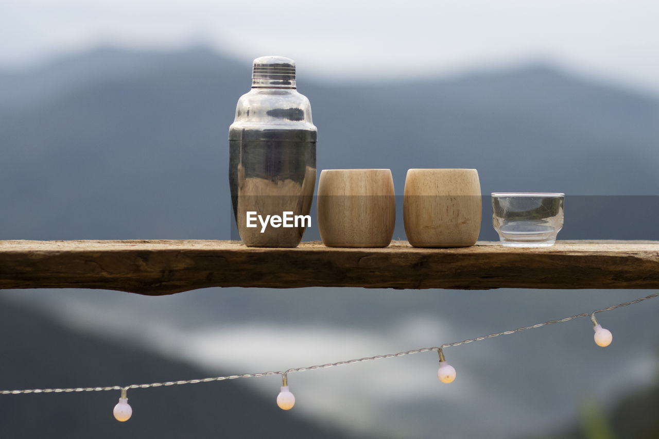 Selective focus stainless steel thermal water bottle and bamboo coffee mug placed on a wooden 