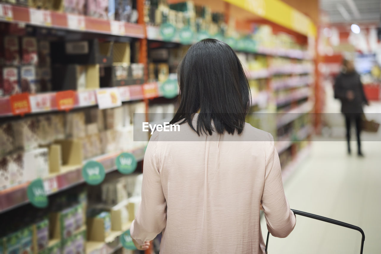 Rear view of woman looking at prices during inflation while doing shopping in supermarket